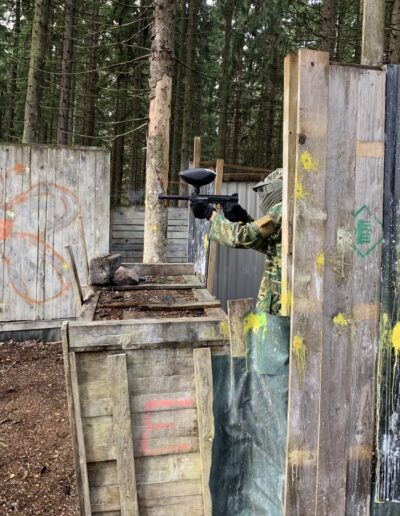 Paintball-pelaaja suojan takana metsäkentällä.