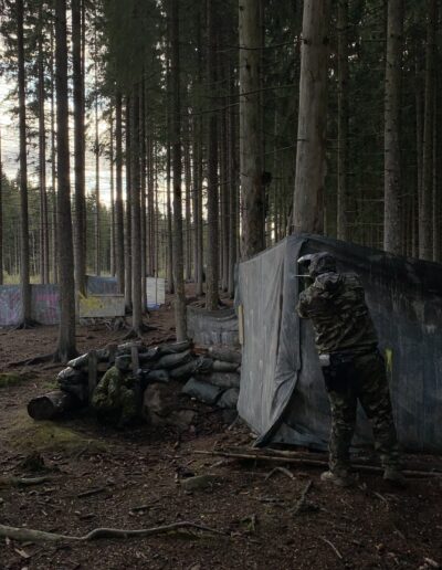 Paintball-pelaaja suojan takana metsäkentällä.